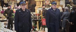 Oficerowie Państwowej Straży Pożarnej w granatowych płaszczach stoją przy trumnie śp. płk. poż. Stanisława Luli. W tle ołtarz, księża i żołnierze w asyście honorowej oraz liczne wieńce kwiatowe.