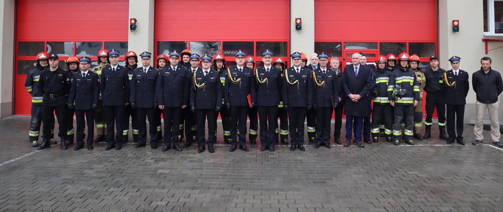 Funkcjonariusze KM PSP Toruń podczas mianowania na nowe stanowiska. Stoją przed budynkiem JRG w Chełmży do pamiątkowego zdjęcia. Ubrani w mundury wyjściowe (galowe).