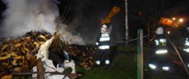 Zdjęcie przedstawia strażaków gaszących pożar sterty porąbanego drewna