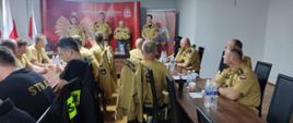 Na zdjęciu funkcjonariusze Państwowej Straży Pożarnej w umundurowaniu służbowym siedzą przy stołach w sali konferencyjnej, przed nimi stoją Komendant Miejski Państwowej Straży Pożarnej w Częstochowie wraz z zastępcą oraz Komendant Centralnej Szkoły Państwowej Straży Pożarnej w Częstochowie wraz z Naczelnikiem Wydziału Działań Ratowniczo-Gaśniczych