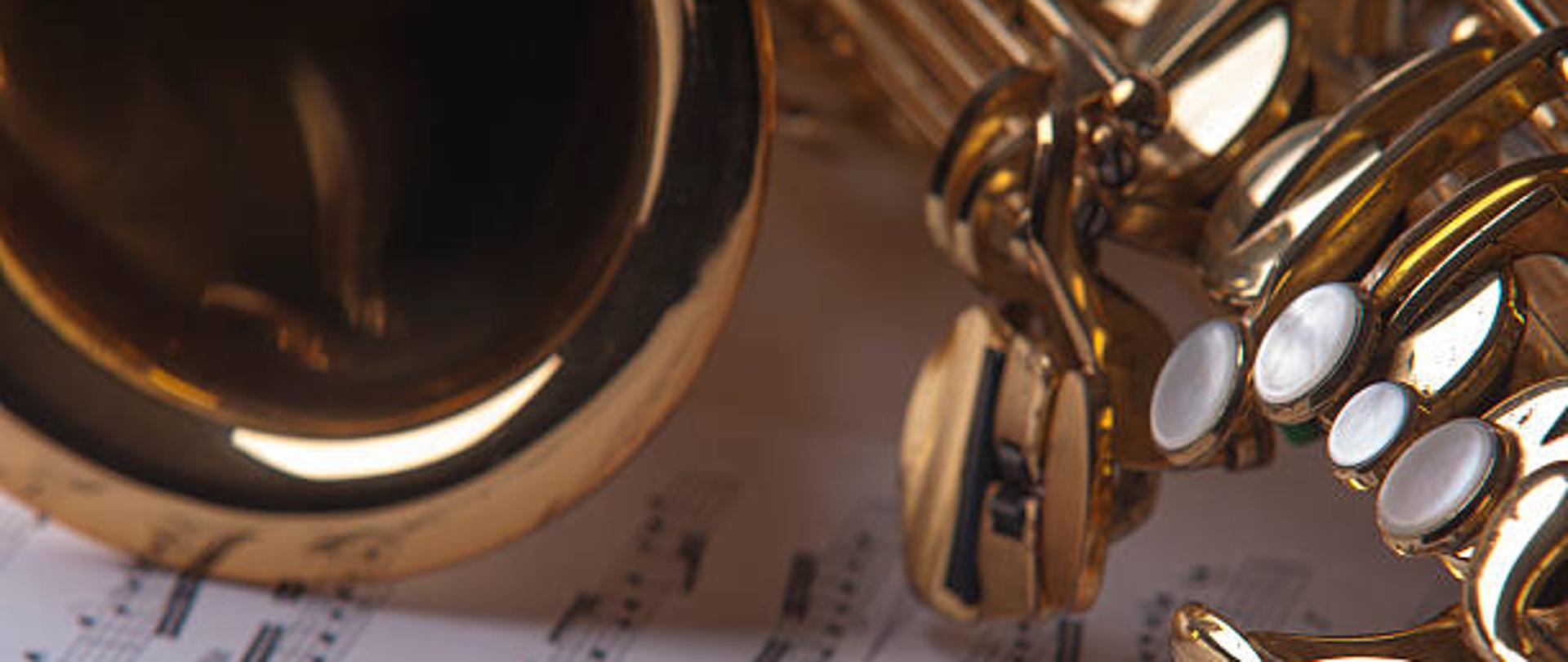 Zdjęcie przedstawiające fragment saksofonu oraz partytury z nutami 