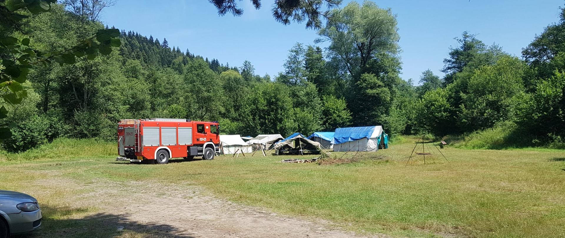 Obóz harcerski na środku polany. Obok samochód strażacki. 