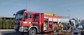 Na zdjęciu widać pojazd ratowniczo-gaśniczy na podwoziu MAN. Pojazd w kolorze czerwonym z oznaczeniami i sygnalizacją ostrzegawczą. Zdjęcie wykonane w ciągu dnia. Słonecznie. Na zdjęciu osoby strażacy ubrani w ubrania specjalne.