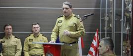Narada roczna podsumowująca funkcjonowanie ochrony przeciwpożarowej w powiecie bielskim za rok 2024 - przemówienie st. bryg. Grzegorza Lisowskiego, w tle 3 funkcjonariuszy KP PSP w Bielsku Podlaskim