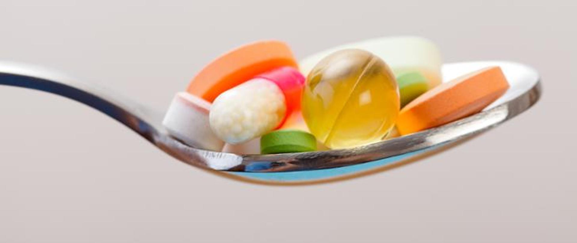 Zdjęcie przedstawia łyżkę stołową wypełnioną tabletkami, kapsułkami - suplementy diety