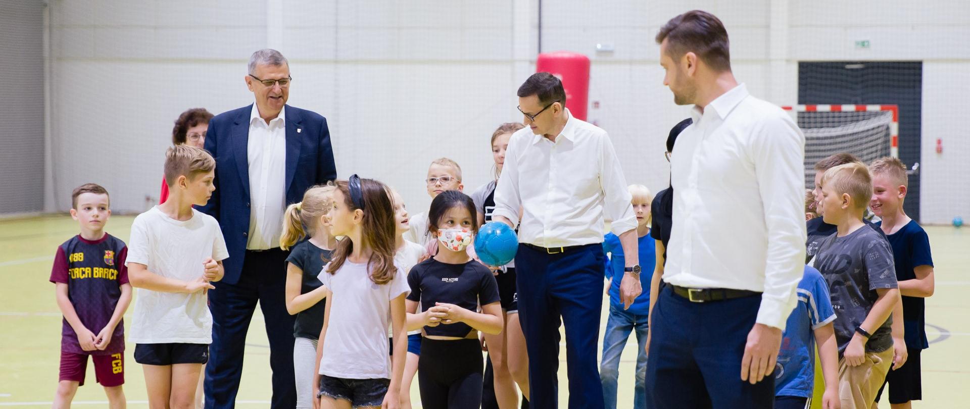 Premier Mateusz Morawiecki i minister sportu i turystyki Kamil Bortniczuk na boisku hali sportowej w Centrum Sportu Raszyn, na boisku z dziećmi.