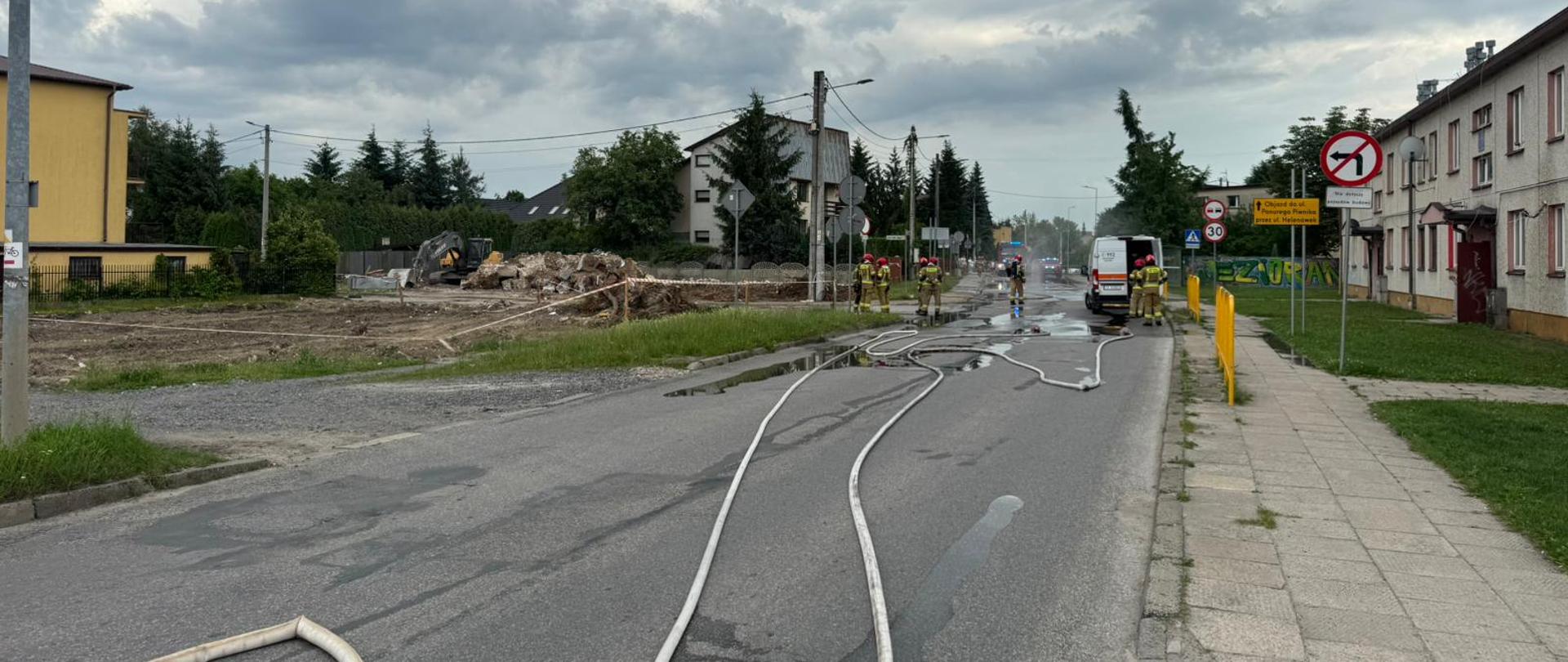 Na zdjęciu ulica Hubalczyków zamknięta dla ruchu, na której rozciągnięto węże gaśnicze zasilające kurtyny wodne. W głębi rozłożone kurtyny oraz samochody służb stojące na drodze. Widać także ratowników przemieszczających się po ulicy.