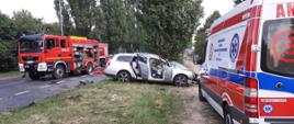 Zniszczony samochód osobowy po wypadku z ciężarówką, w tle pojazdy straży pożarnej i pogotowia