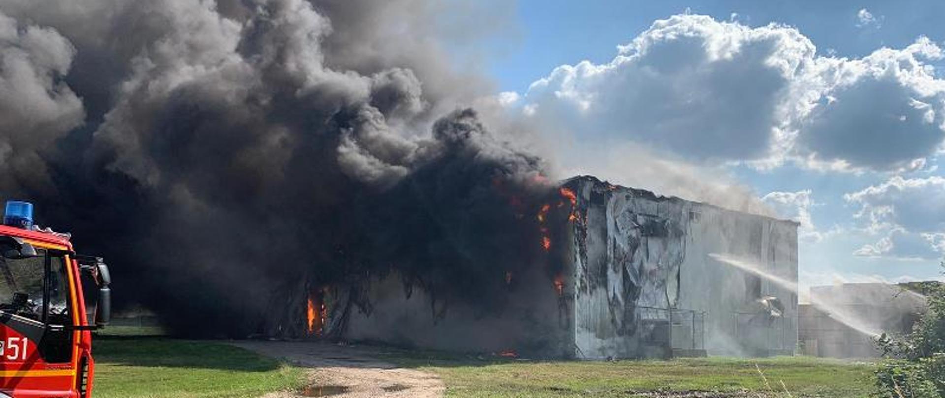 Na zdjęciu widać pożar hali, duży dym oraz częściowo samochód pożarniczy.