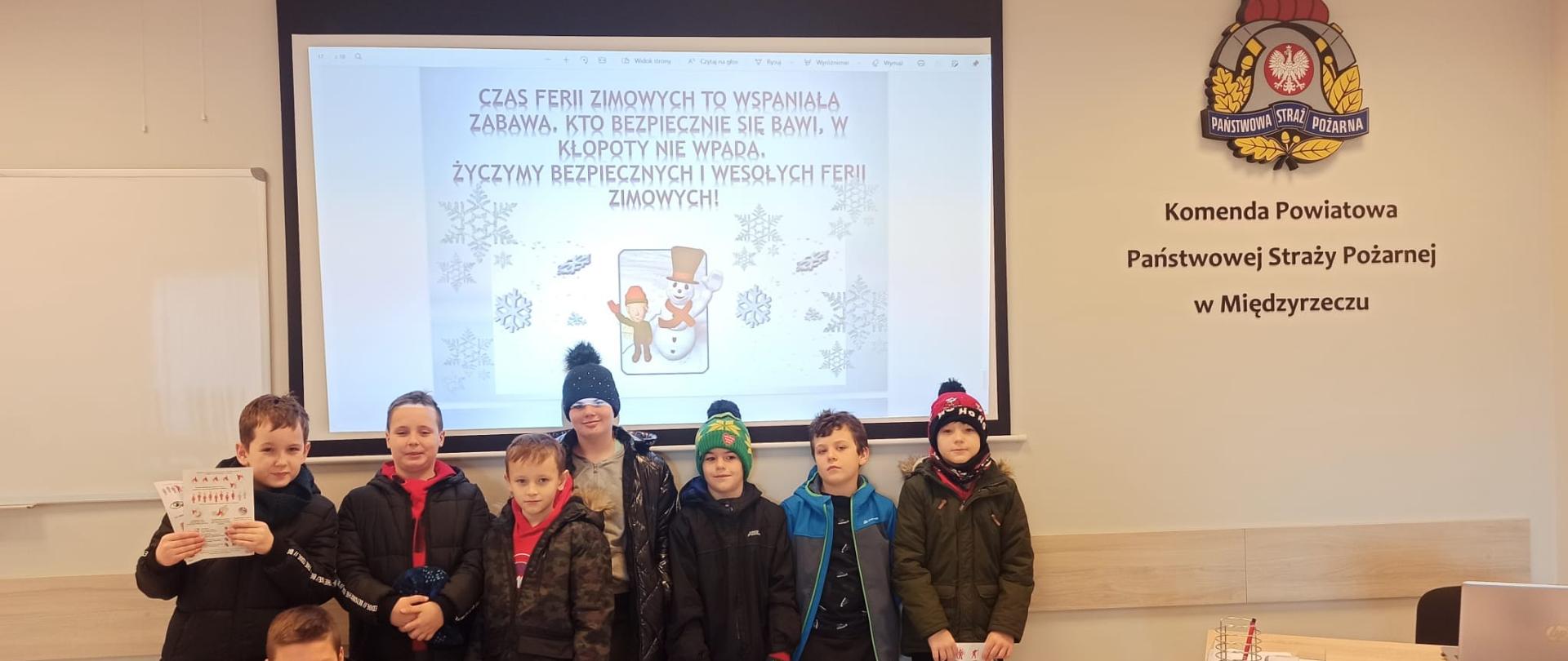 Zdjęcie przedstawia grupę dzieci na świetlicy w budynku Komendy Powiatowej PSP w Międzyrzeczu podczas oglądania prezentacji multimedialnej dotyczącej bezpieczeństwa.