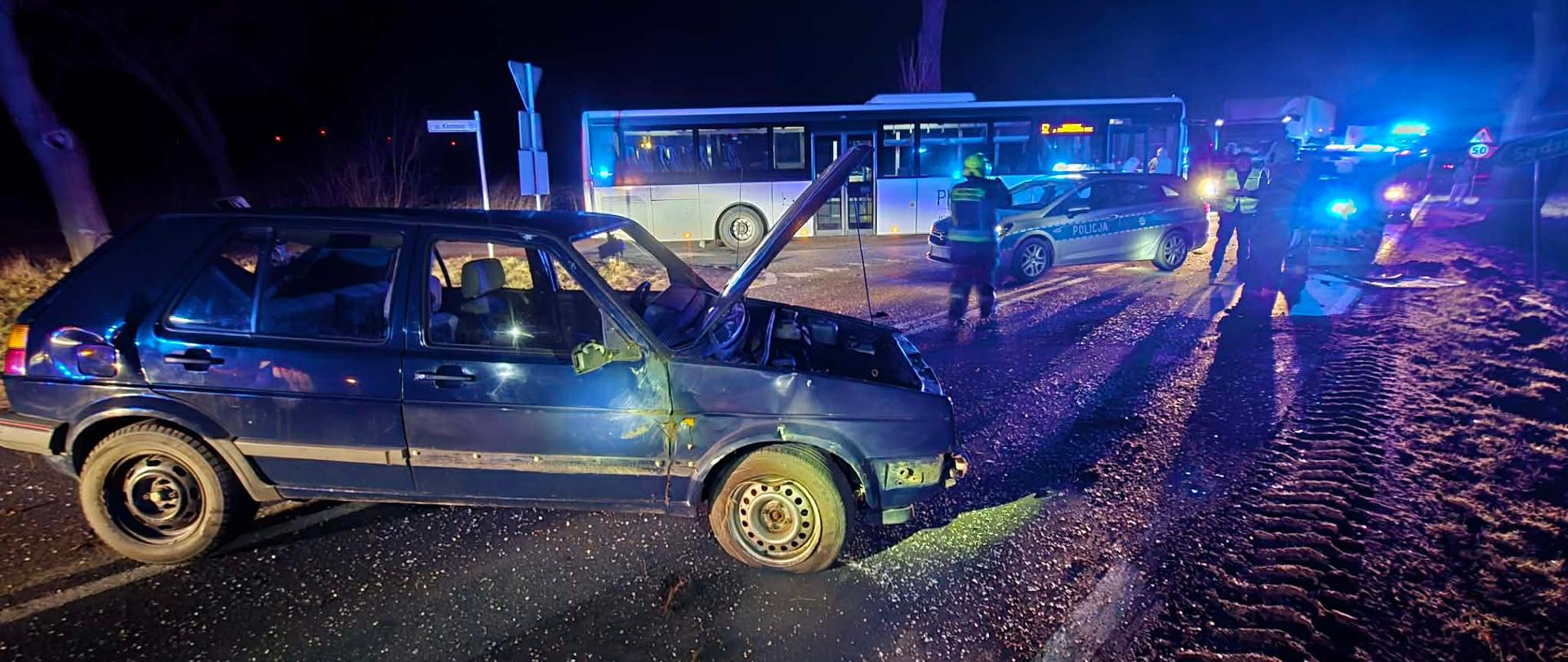 Samochód na drodze, za nim autobus, jest ciemno