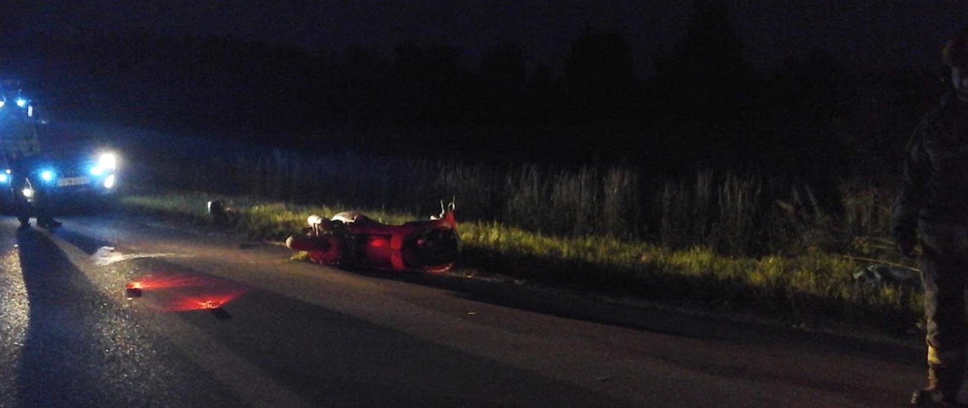 Skuter leżący na jezdni po zderzeniu z sarną. Miejsce zdarzenia oznakowane przy użyciu flar świetlnych.