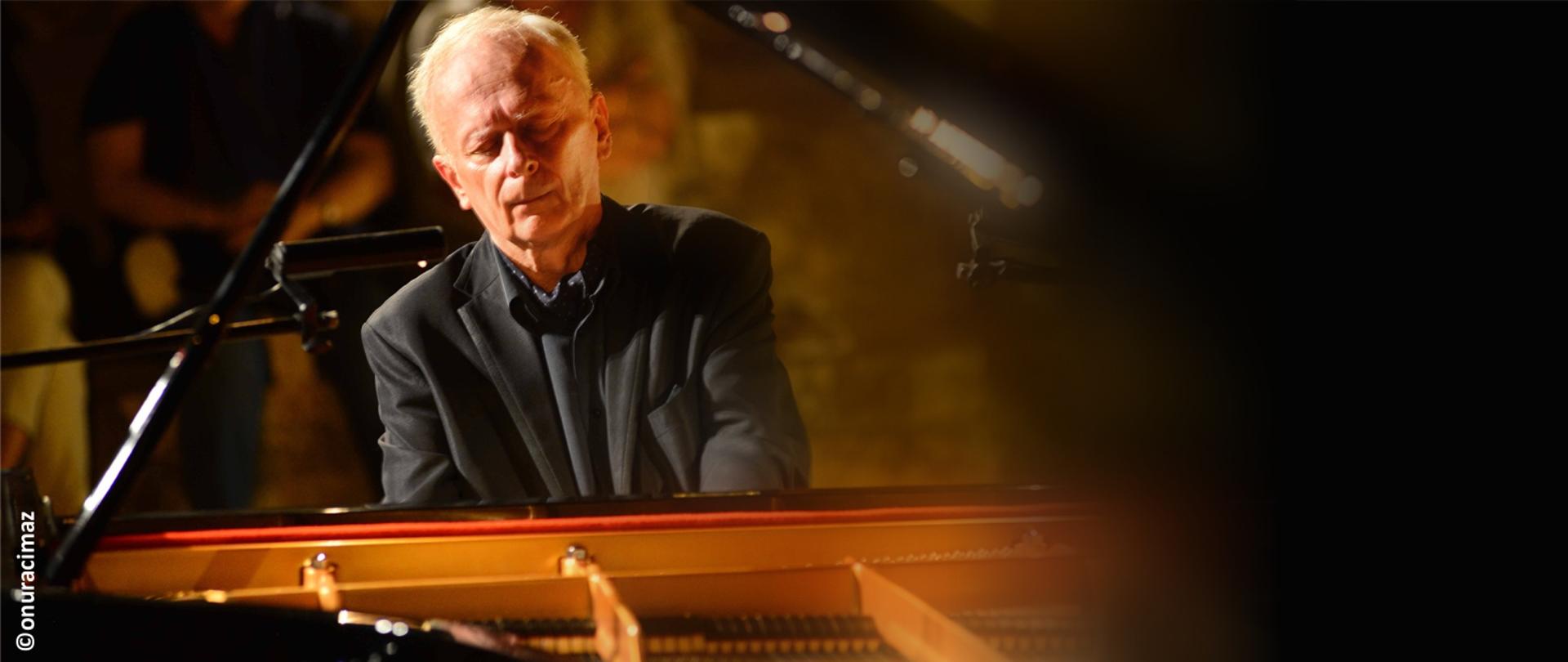 Zdjęcie przedstawia Janusza Olejniczaka grającego na fortepianie
