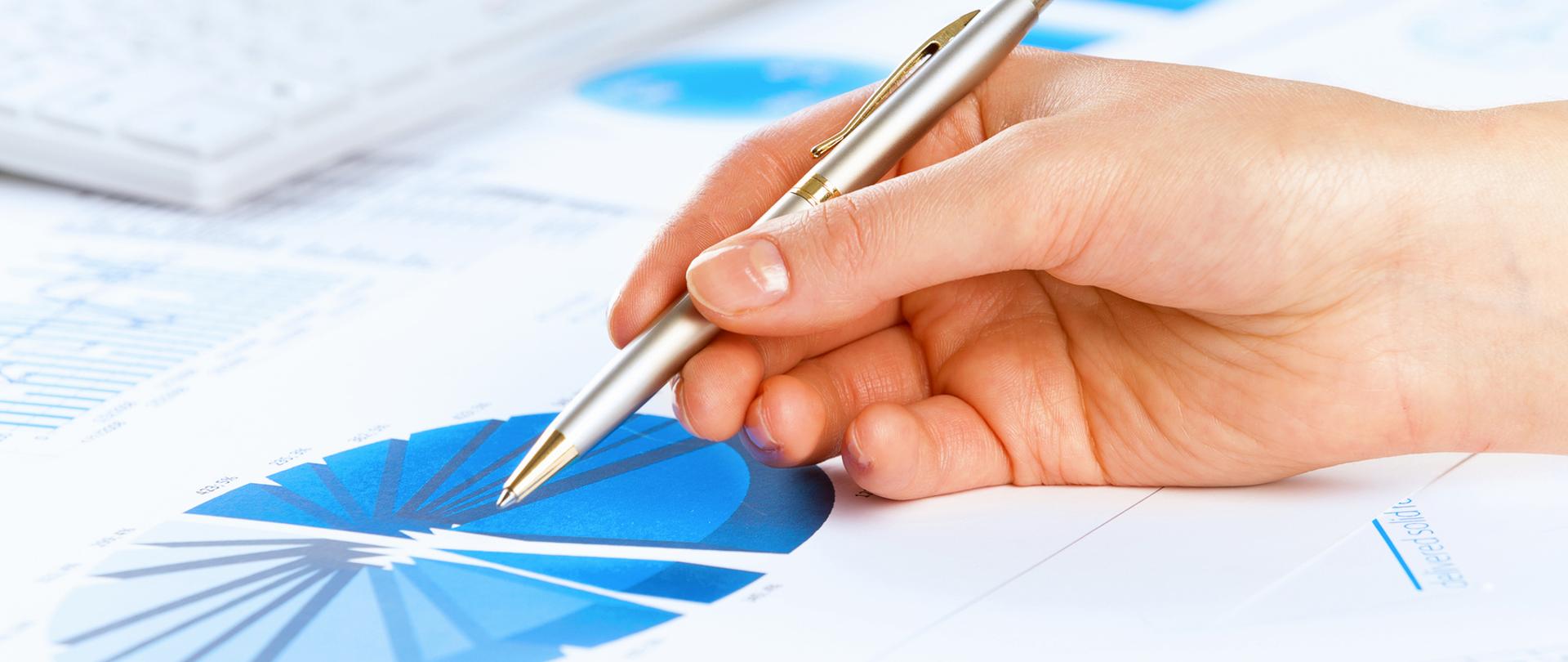 Dłoń w której widać długopis dotykający grafu z danymi 