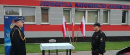 Na zdjęciu Komendant Powiatowy Państwowej Straży Pożarnej w Złotowie mł.bryg. Jarosław Kołak oraz Dowódca Jednostki Ratowniczo Gaśniczej st.kpt. Krzysztof Olczak. Dowódca JRG składa meldunek Komendantowi o rozpoczęciu uroczystości ślubowania. W tle widoczny jest budynek JRG, Flagi Państwowe.