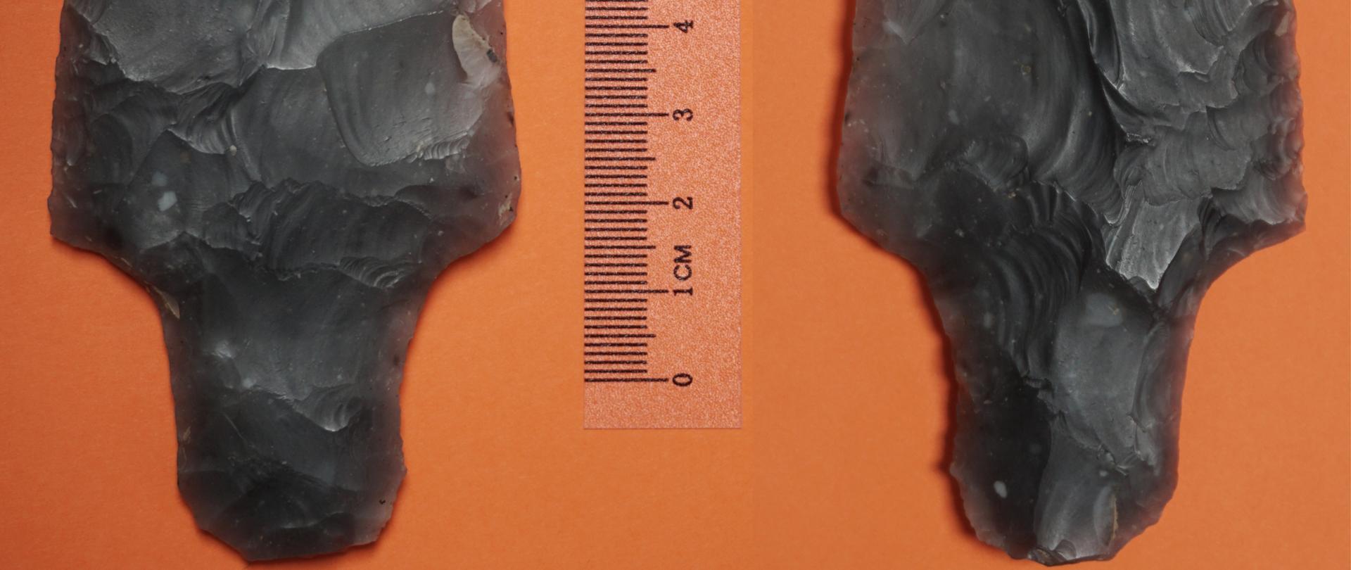 fotografia przedstawia krzemienny grot na pomarańczowym tle