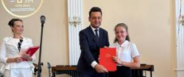 Poseł Przemysław Witek, Pani Dyrektor Sonia Wachowska oraz nagrodzony uczeń na scenie w sali koncertowej podczas Uroczystego Koncertu Absolwentów w Państwowej Szkole Muzycznej I st. w Lublińcu