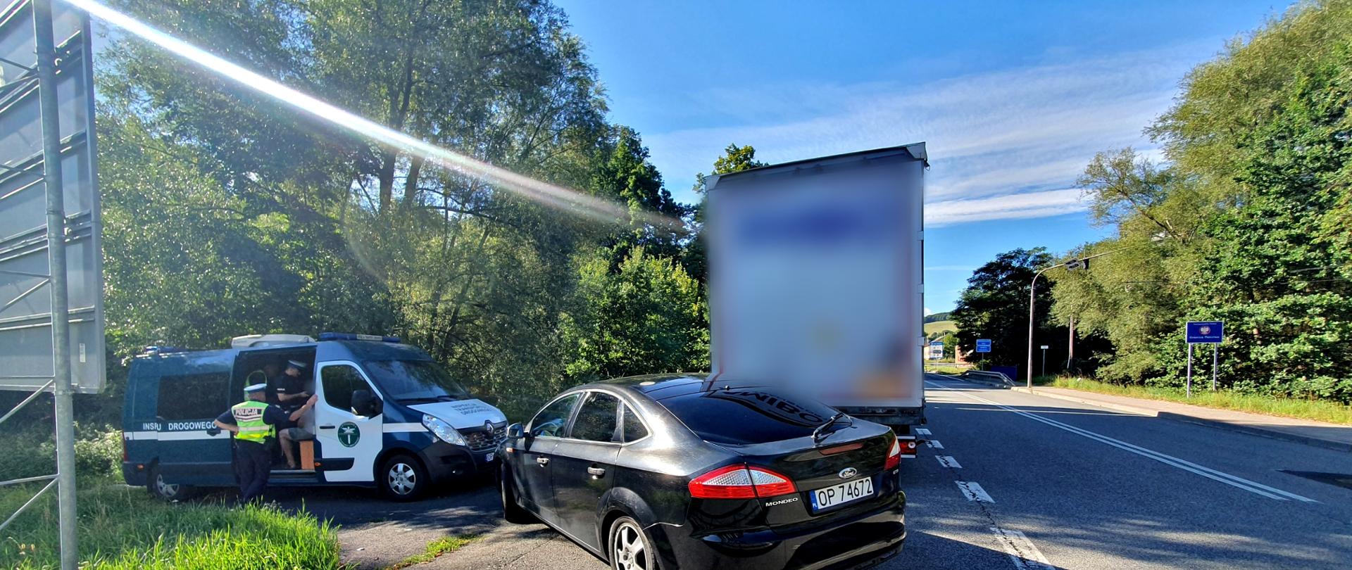 Funkcjonariusz Policji przy oznakowanym pojeździe Inspekcji Transportu Drogowego. Obok stoją samochód osobowy oraz kontrolowany pojazd ciężarowy.