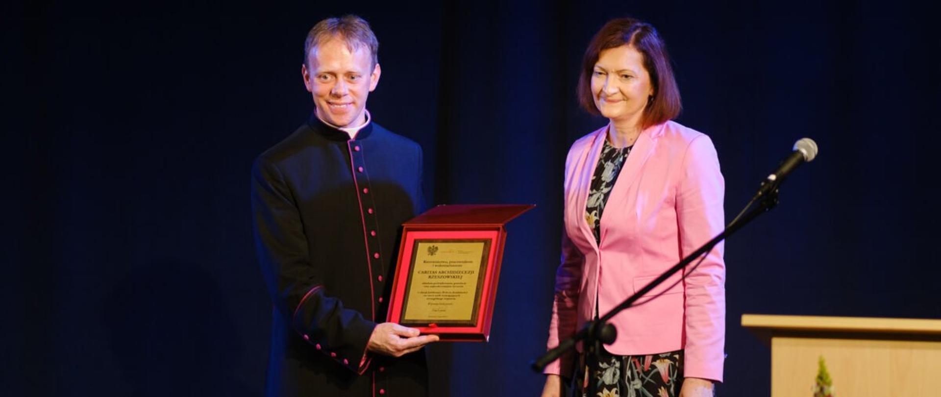Od lewej ks. Piotr Potyrała trzymający pamiątkowy grawerton, obok wojewoda podkarpacki Ewa Leniart.