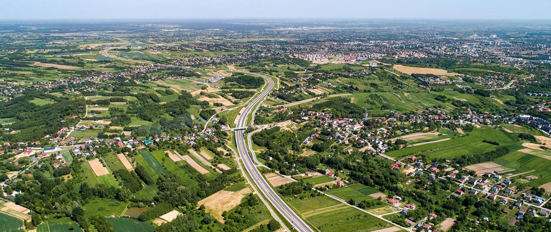 Widok z góry na drogę krajową. W tle widoczne zabudowania i pola uprawne.