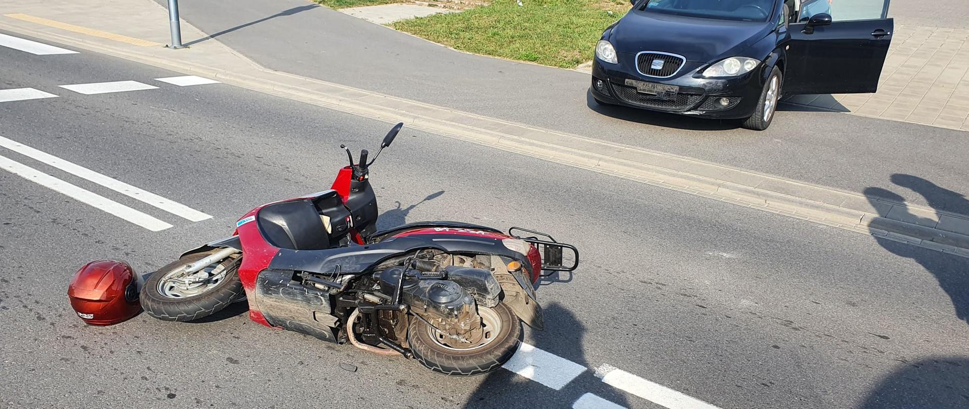 Jednoślad na drodze. Droga asfaltowa. Kolor szary. Zdjęcie w ciągu dnia. Słonecznie. Pojazd leży na boku.
