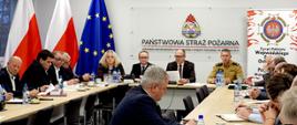 Na zdjęciu widać spotkanie posiedzenie Prezydium Zarządu Oddziału Wojewódzkiego Związku Ochotniczych Straży Pożarnych RP województwa śląskiego w sali Komendy Wojewódzkiej Państwowej Straży Pożarnej w Katowicach. Przy długim stole w kształcie prostokąta siedzi kilkanaście osób – głównie mężczyźni w garniturach, a także jedna kobieta. Na środku stołu, po stronie głównej, siedzi mężczyzna w okularach i garniturze, który trzyma kartkę i prawdopodobnie prowadzi zebranie. Obok niego znajduje się mężczyzna w piaskowym mundurze służbowym - Jest to st. bryg. Roman Klecha - Zastępca Śląskiego Komendanta Wojewódzkiego. Na ścianie za nimi widnieje duże logo Państwowej Straży Pożarnej oraz napis „Komenda Wojewódzka Państwowej Straży Pożarnej w Katowicach”. Obok stoi roll-up z emblematem Ochotniczych Straży Pożarnych RP i napisem o wojewódzkim zarządzie związku. Z lewej strony sali widać flagi Polski i Unii Europejskiej. Na stołach leżą notatniki, dokumenty, długopisy, filiżanki z kawą i butelki z wodą. 