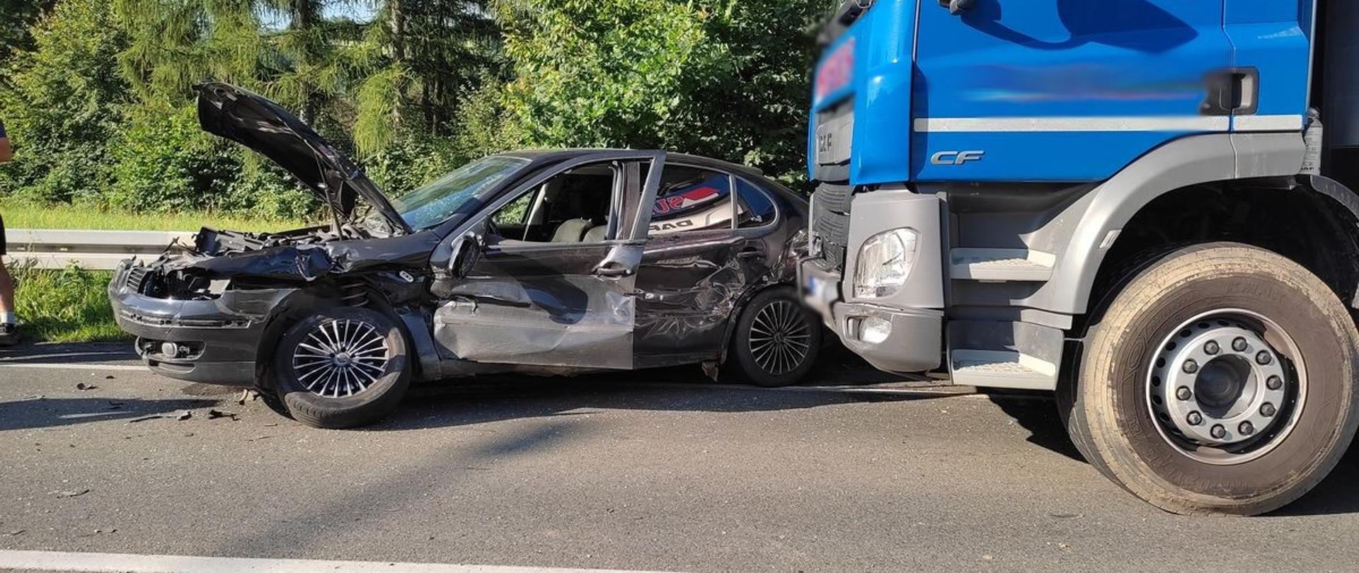 Uszkodzony samochód osobowy koloru ciemnego a za nim samochód ciężarowy