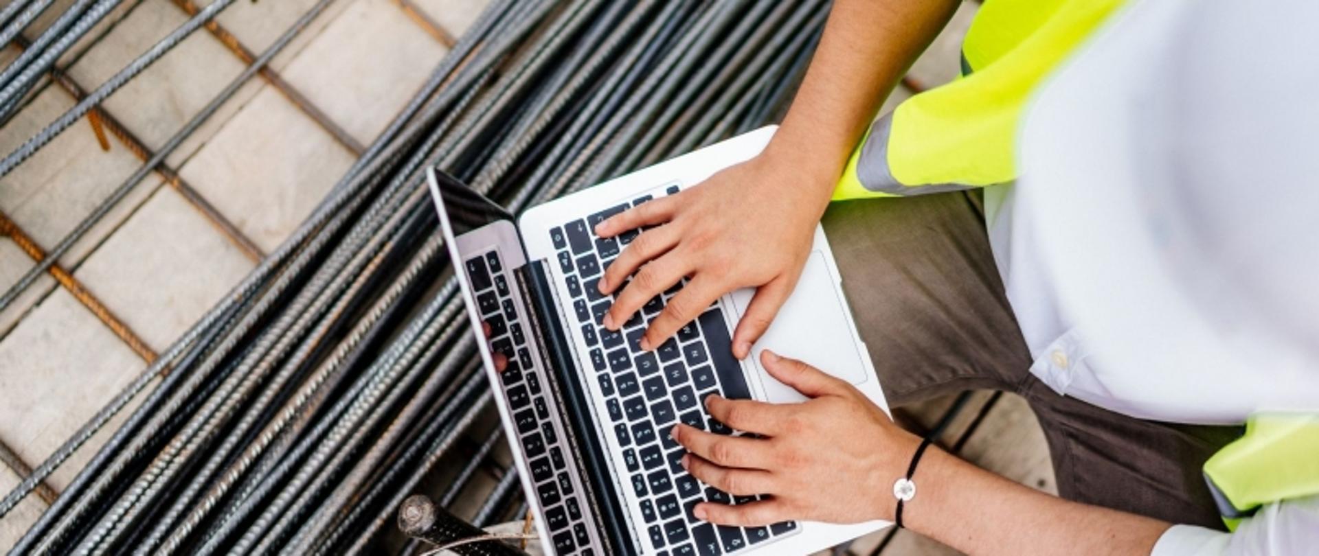 Człowiek na budowie piszący na laptopie.