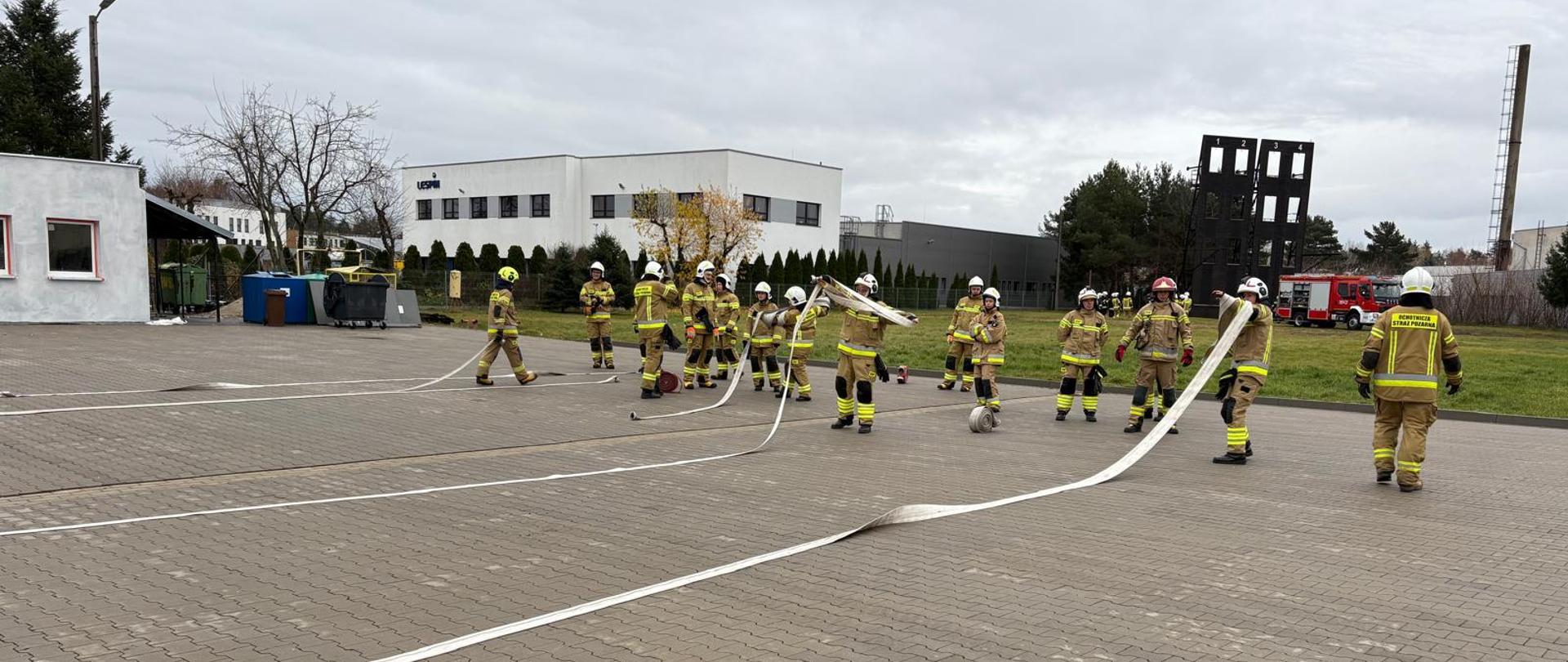 Strażacy uczą się zwijania węży pożarniczych na placu komendy.