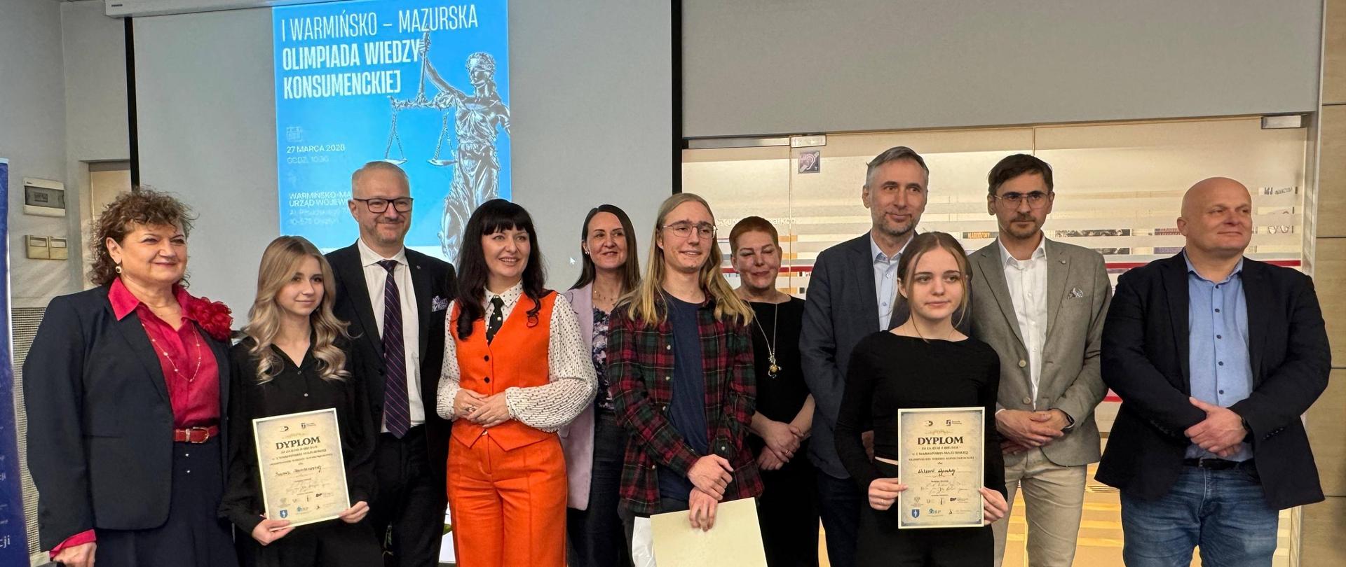 Mężczyzna w garniturze, wojewoda, podaje rękę dziewczynce, gratulując 