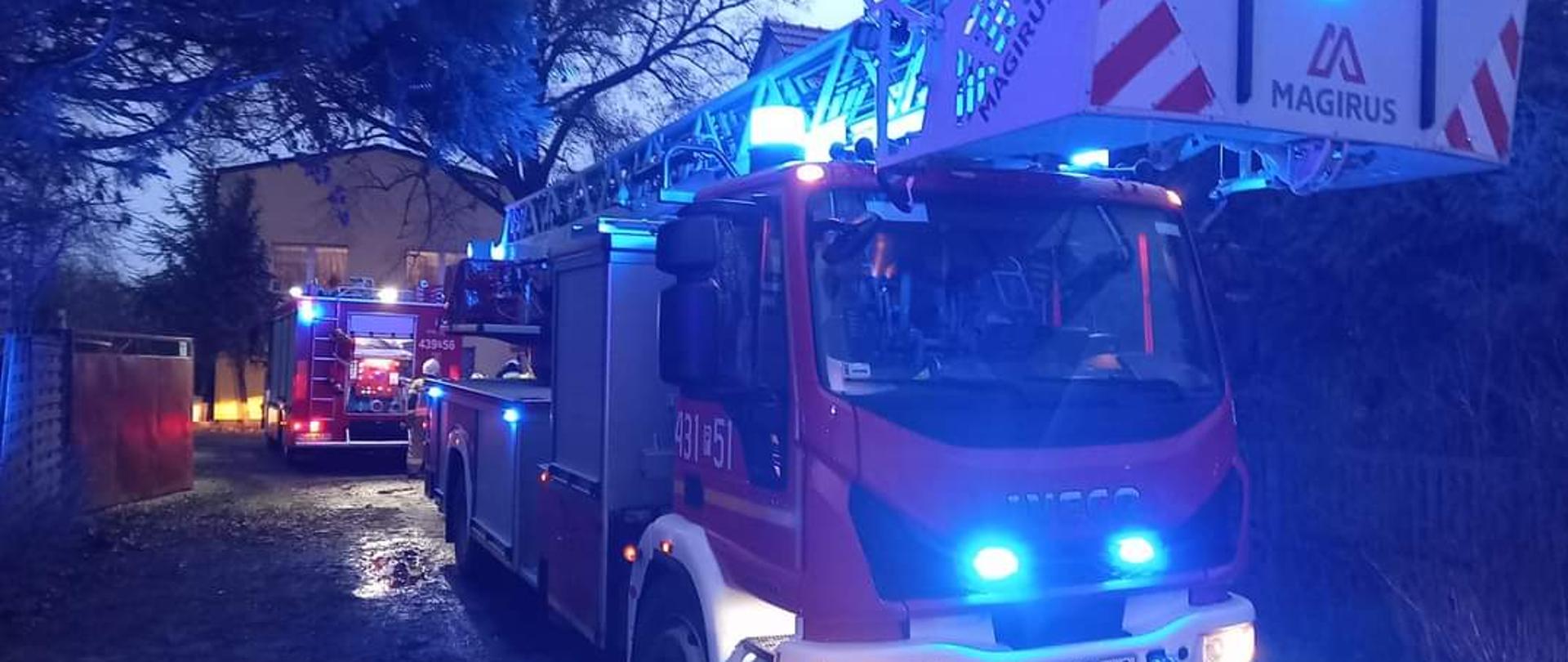 Na zdjęciu widać samochód pożarniczy z włączonymi niebieskimi światłami. Samochód bierze udział w działaniach ratowniczo-gaśniczych.