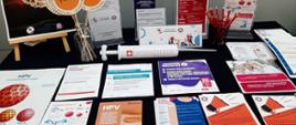 Widok stoiska edukacyjnego z rozłożonymi ulotkami dotyczącymi HPV
