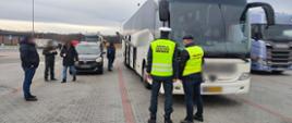 Umundurowani funkcjonariusze śląskiej Inspekcji Transportu Drogowego i Straży Granicznej stoją obok kontrolowanego autobusu dalekobieżnego.