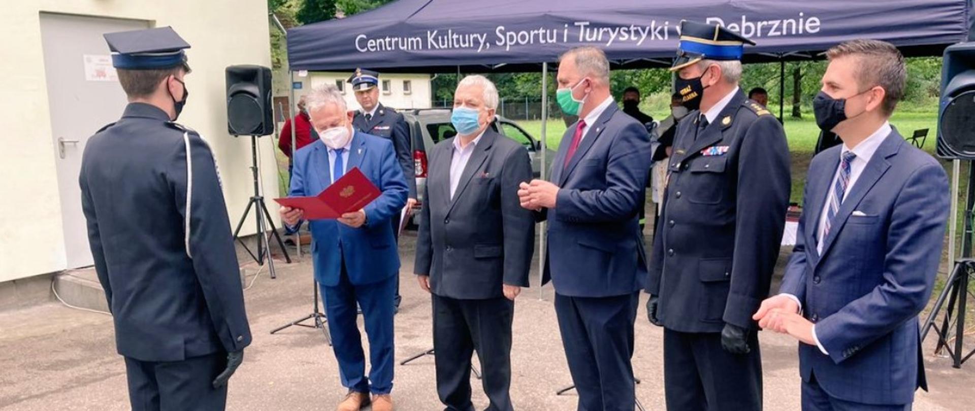 Przekazanie wozu strażackiego w Starym Granowie. Komendant Powiatowy PSP w Człuchowie odbiera akt przekazania wozu od posła Pana Aleksandra Mrówczyńskiego. Na zdjęci zgromadzeni są również przedstawiciele władz samorządowych oraz Pomorski Komendant Wojewódzki PSP st. bryg. Piotr Socha. W tle znajduje się parasol z napisem Centrum Kultury, Sportu i Turystyki w Debrznie. 