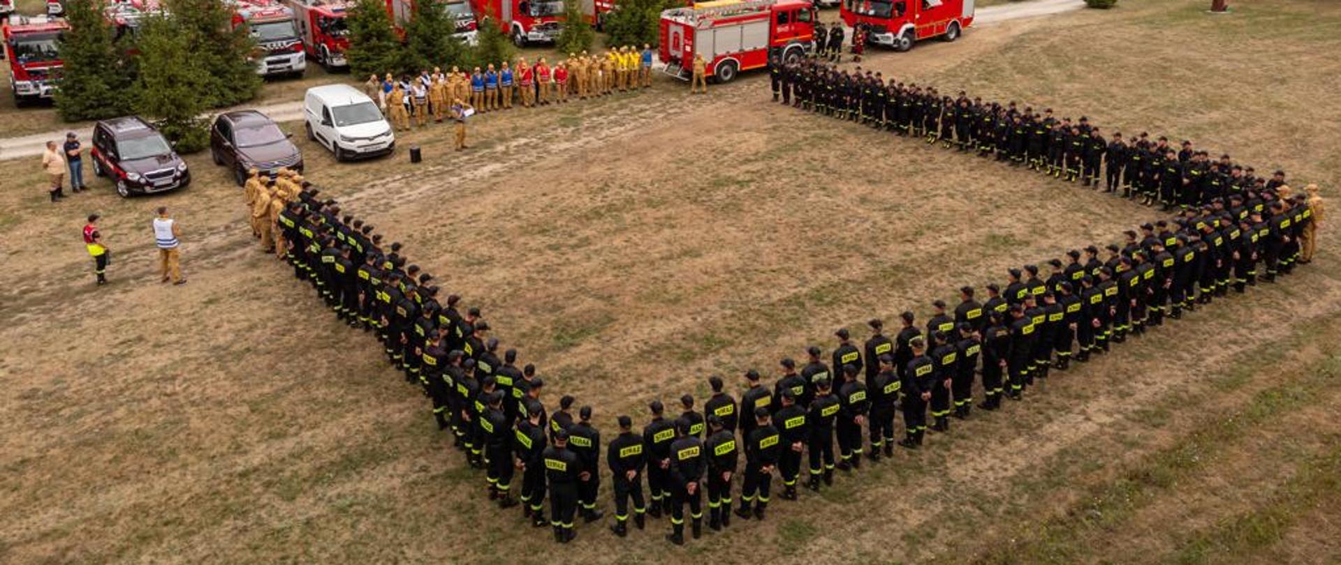 Na zdjęciu widzimy samochody pożarnicze zaparkowane w punkcie przyjęcia sił i środków oraz strażaków, którzy uczestniczyli w ćwiczeniach.