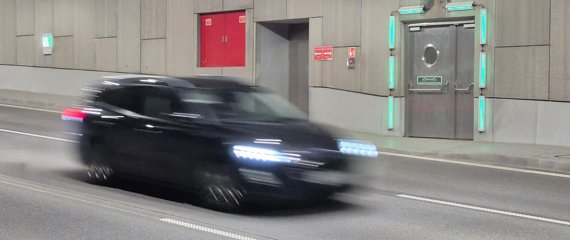 Samochód osobowy w tunelu na Północnej Obwodnicy Krakowa, na ścianie tunelu przejście awaryjne
