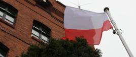 Na maszcie powiewa flaga biało-czerwona. W tle wieża budynku strażnicy.
