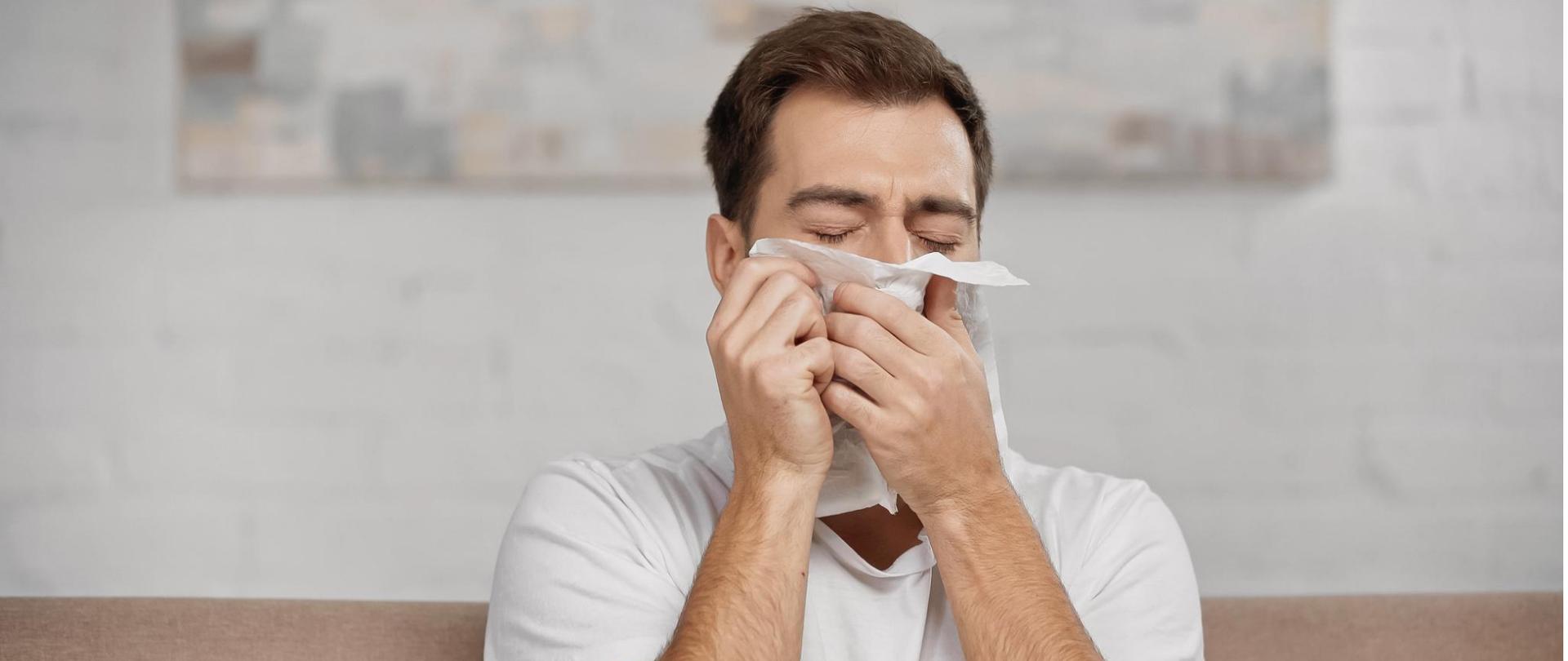 Na zdjęciu jest mężczyzna wycierający nos chusteczką higieniczną. 
