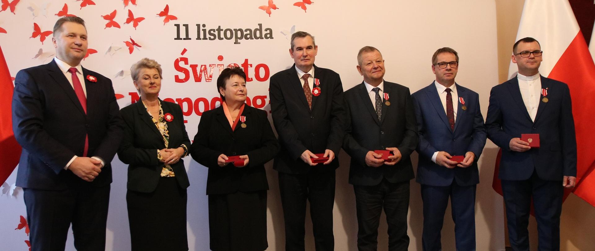 Zdjęcie zbiorowe, pod ścianą z napisem 11 listopada święto niepodległości stoi minister Czarnek i kilka elegancko ubranych osób.