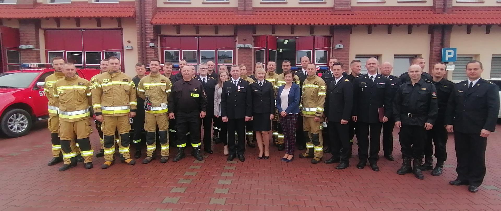 Zdjęcie przedstawia uroczystą zmianę służby na której odbyło się pożegnanie funkcjonariusza, który odszedł na emeryturę. Na zdjęciu widzimy funkcjonariuszy oraz pracowników cywilnych Komendy Powiatowej PSP w Ostrzeszowie.
Zdjęcie wykonane w porze dziennej przed budynkiem Komendy Powiatowej PSP.