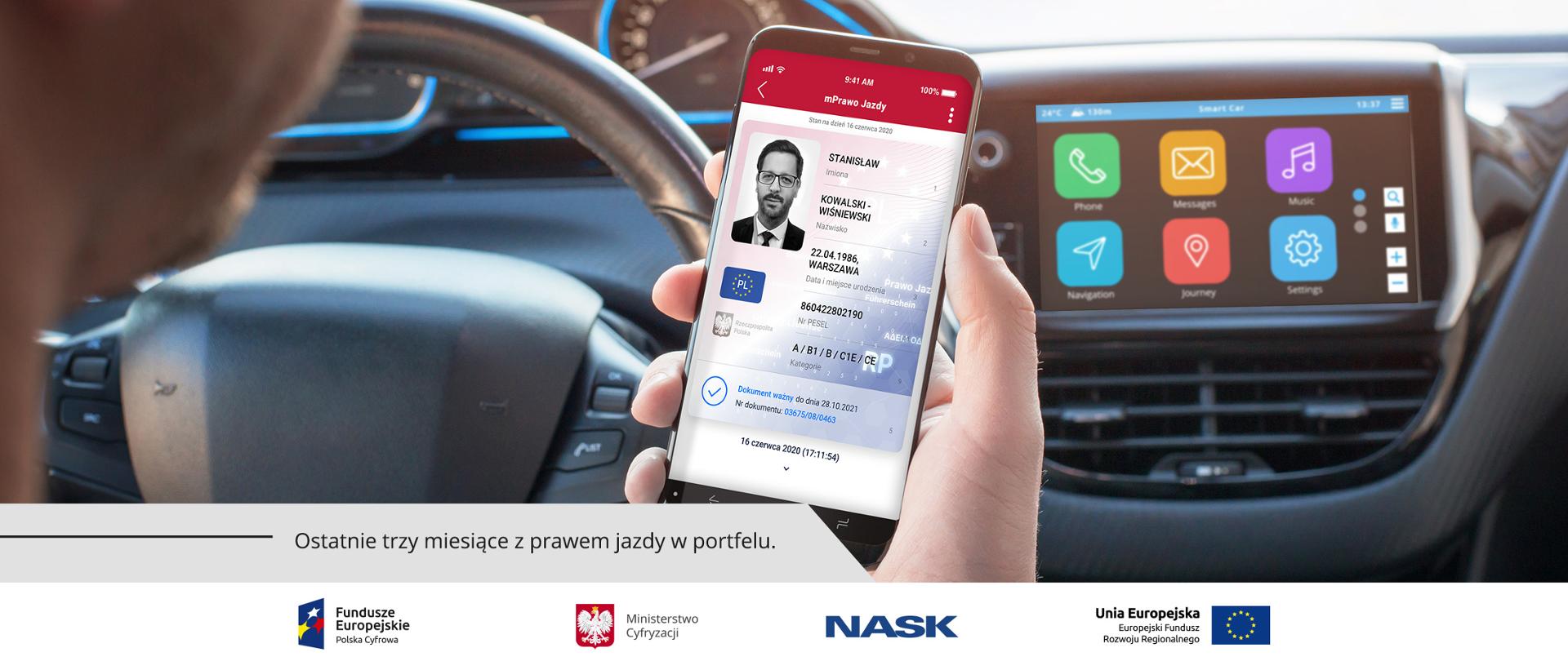 Kierowca trzyma w ręku telefon komórkowy, na jego ekranie wyświetla się mPrawo Jazdy.