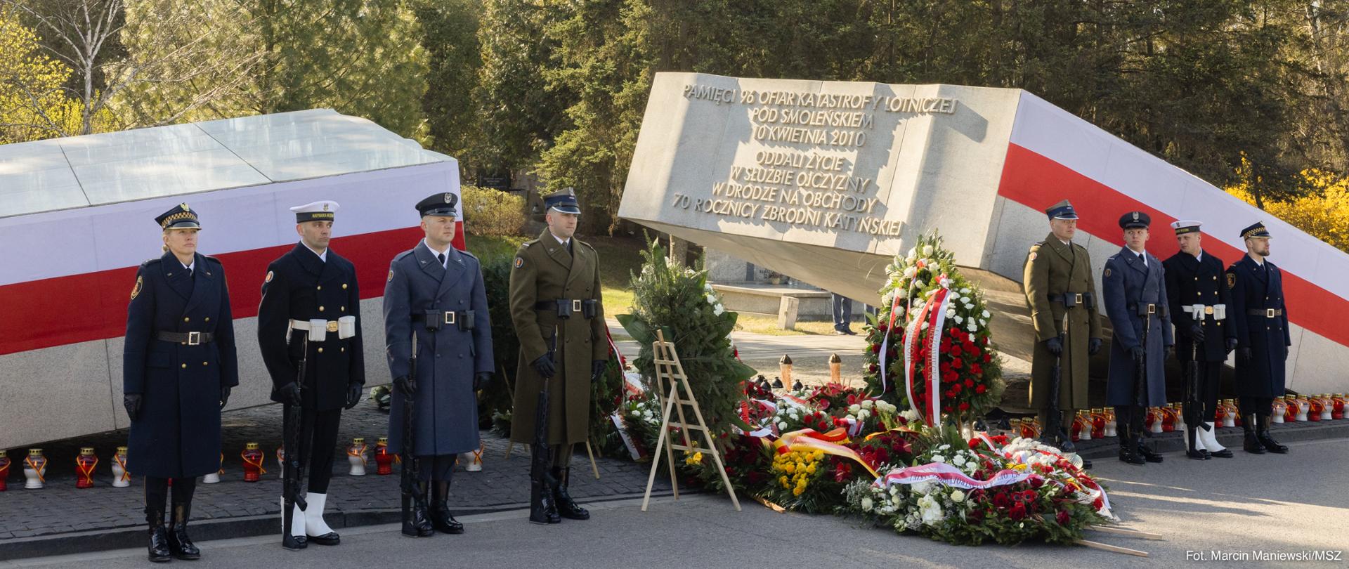 The photo shows men in uniform standing by a monument.There are wreaths next to them. 