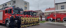 Funkcjonariusze Komendy, stojący na placu przed samochodami strażackimi obok masztu flagowego śpiewają hymn państwowy.