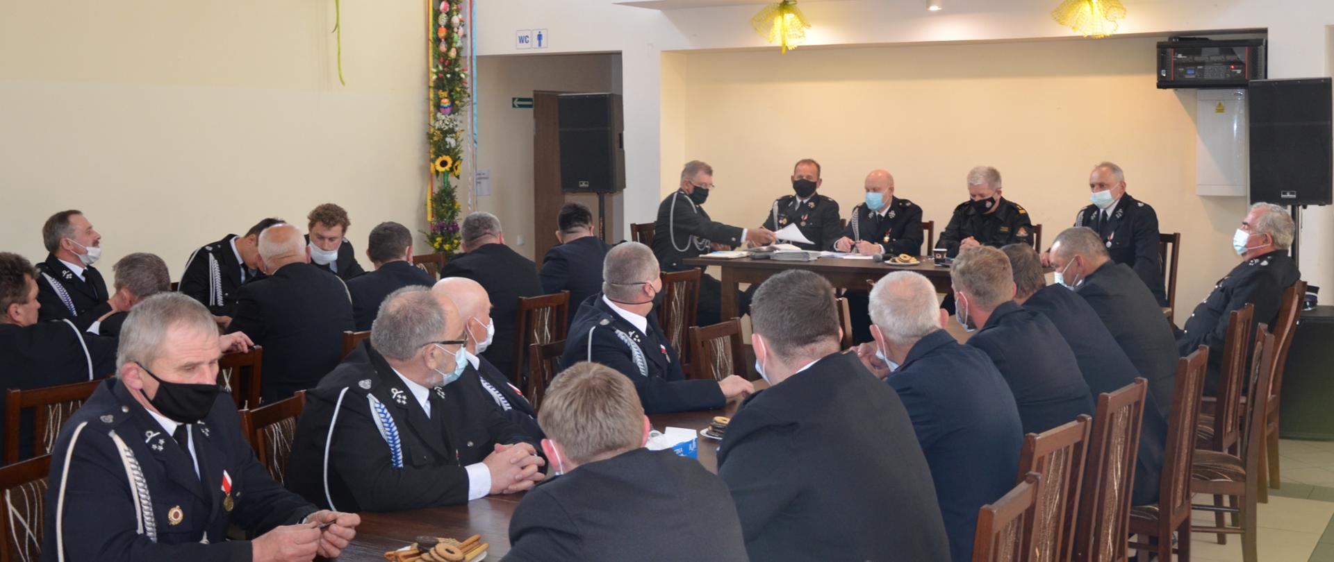 Zdjęcie przedstawia druhów osp siedzących przy stołach na sali podczas konsultacji społecznych dotyczących projektu ustawy o osp, w tle stół prezydialny z Komendantem Powiatowym PSP w Wieluniu