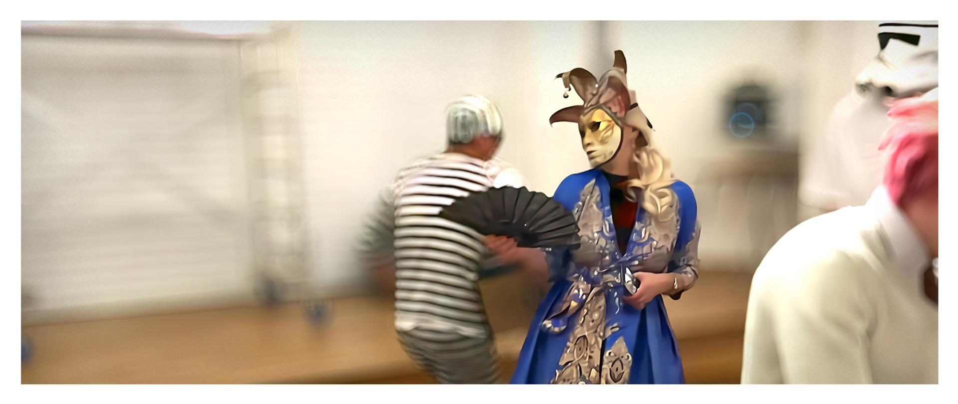 kobieta w masce karnawałowej, w tle mężczyzna przebrany w więzienny strój w paski