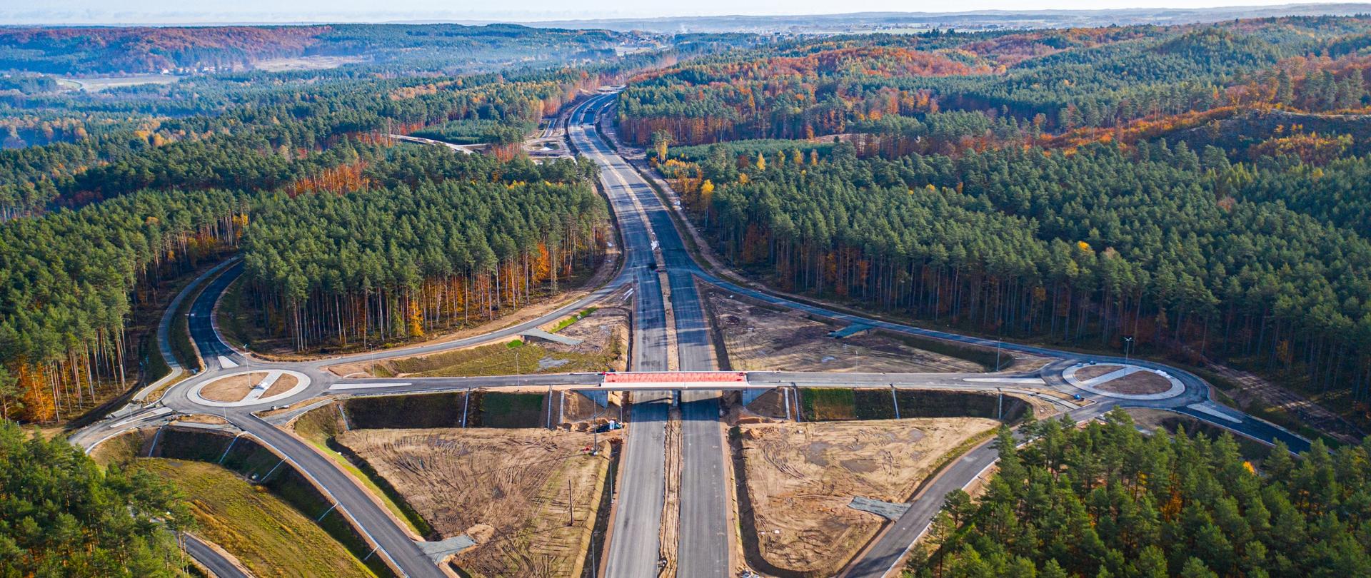 Zdjęcie przedstawia widok z lotu ptaka na budowany węzeł drogi ekspresowej S6 w Strzebielinie. W centrum są jezdnie główne drogi ekspresowej, nad nimi wiadukt, a po bokach łącznice i ronda łączące trasę z drogami poprzecznymi.