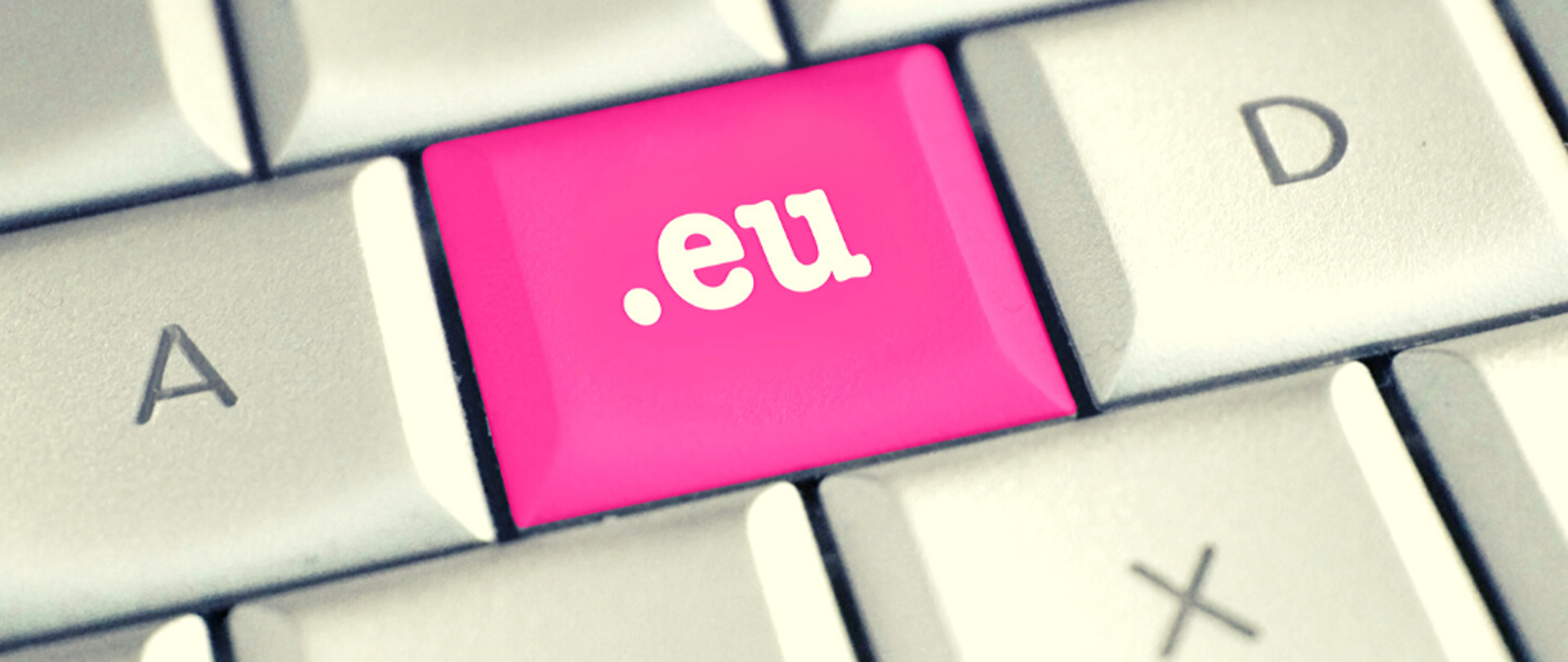 Wąski ujęcie klawiatury. Widać kilka klawiszy, z których większość jest biała z czarnymi literami. Na środku różowy klawisz z białym napisem .eu