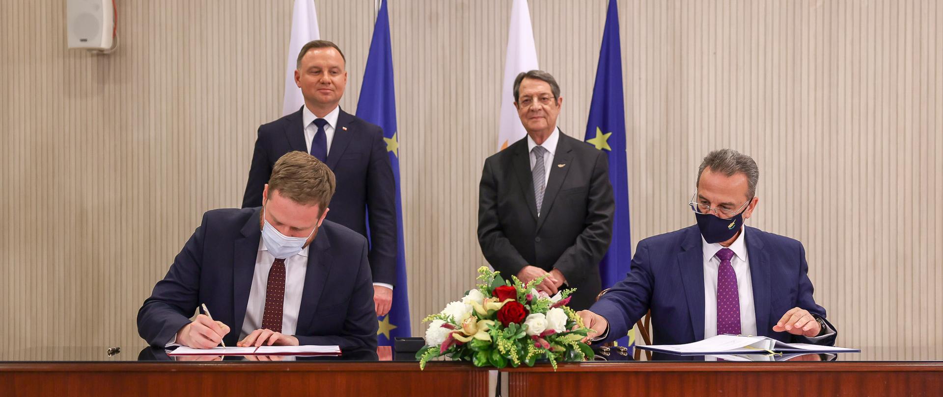 Ministrowie Janusz Cieszyński i Kyriacos Kokkinos podczas podpisywania porozumienia. Za nimi prezydenci Polski i Cypru.