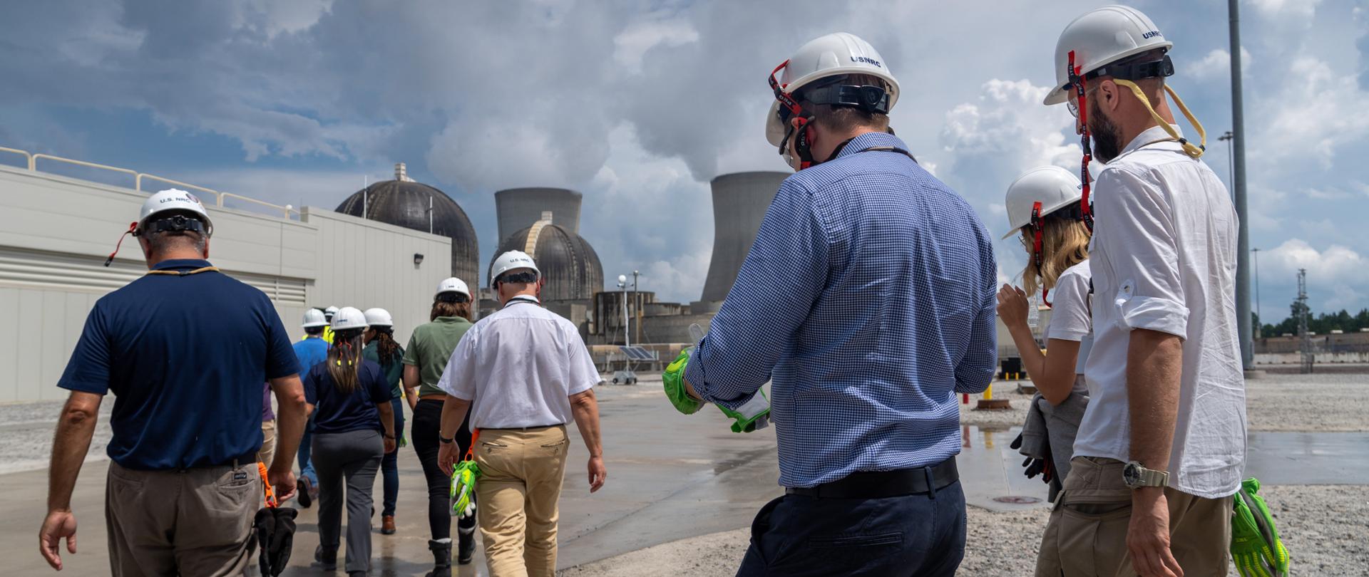 Wizyta delegacji PAA w Elektrowni Jądrowej Vogtle 2 - uczestnicy w kaskach ochronnych kierują się w stronę budynków reaktorów