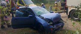 Dzień. Na pierwszym planie uszkodzony Ford Focus, w tle strażacy i karetka pogotowia ratunkowego.